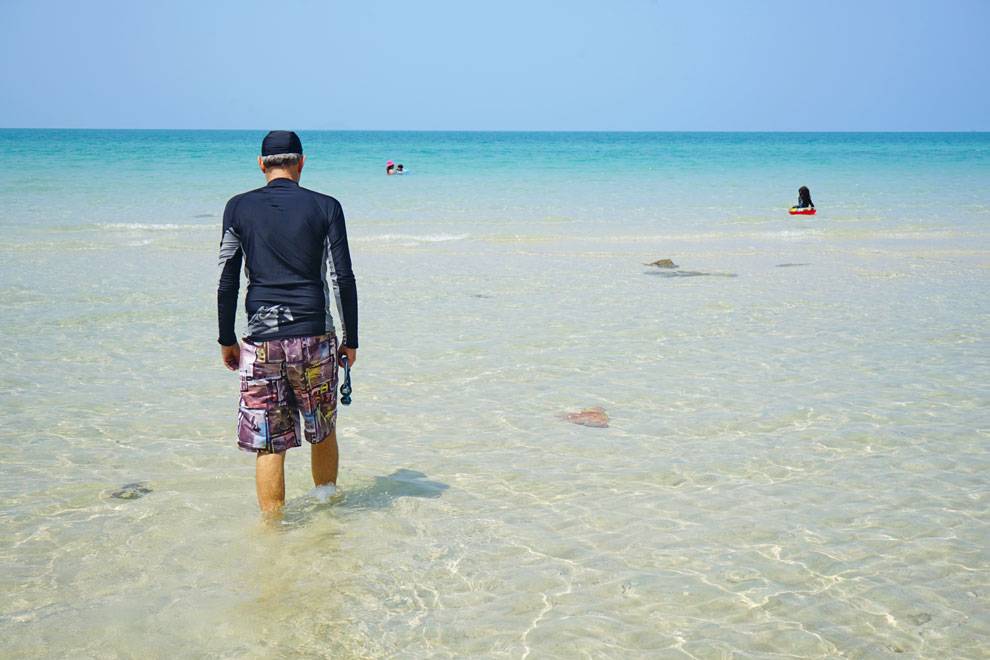 Hombre entrando en las transparentes aguas de Sai Kaew Entrando al agua